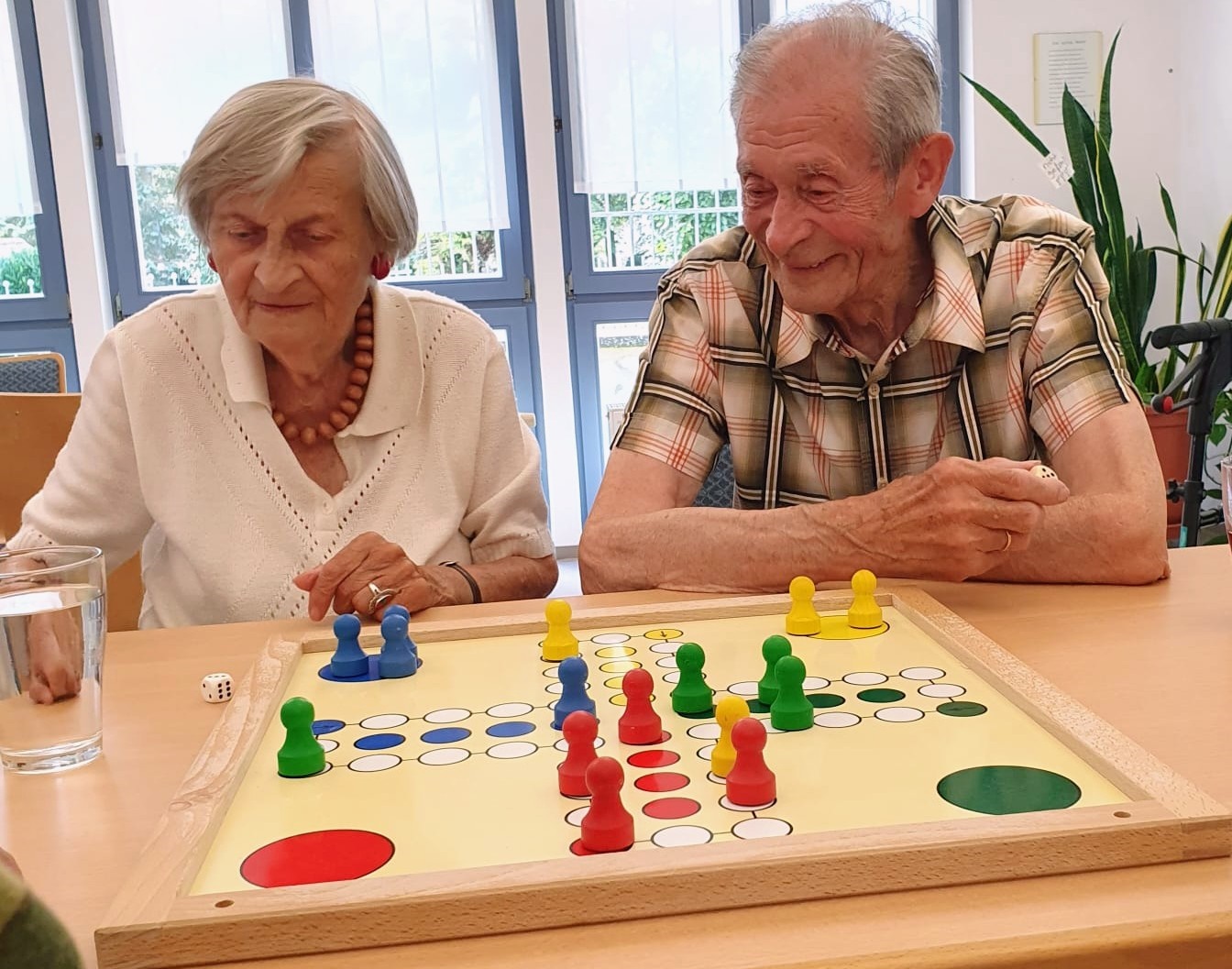 zwei &auml;ltere Menschen sitzen am Tisch. Vor ihnen liegt ein Brettspiel mit mehreren Figuren