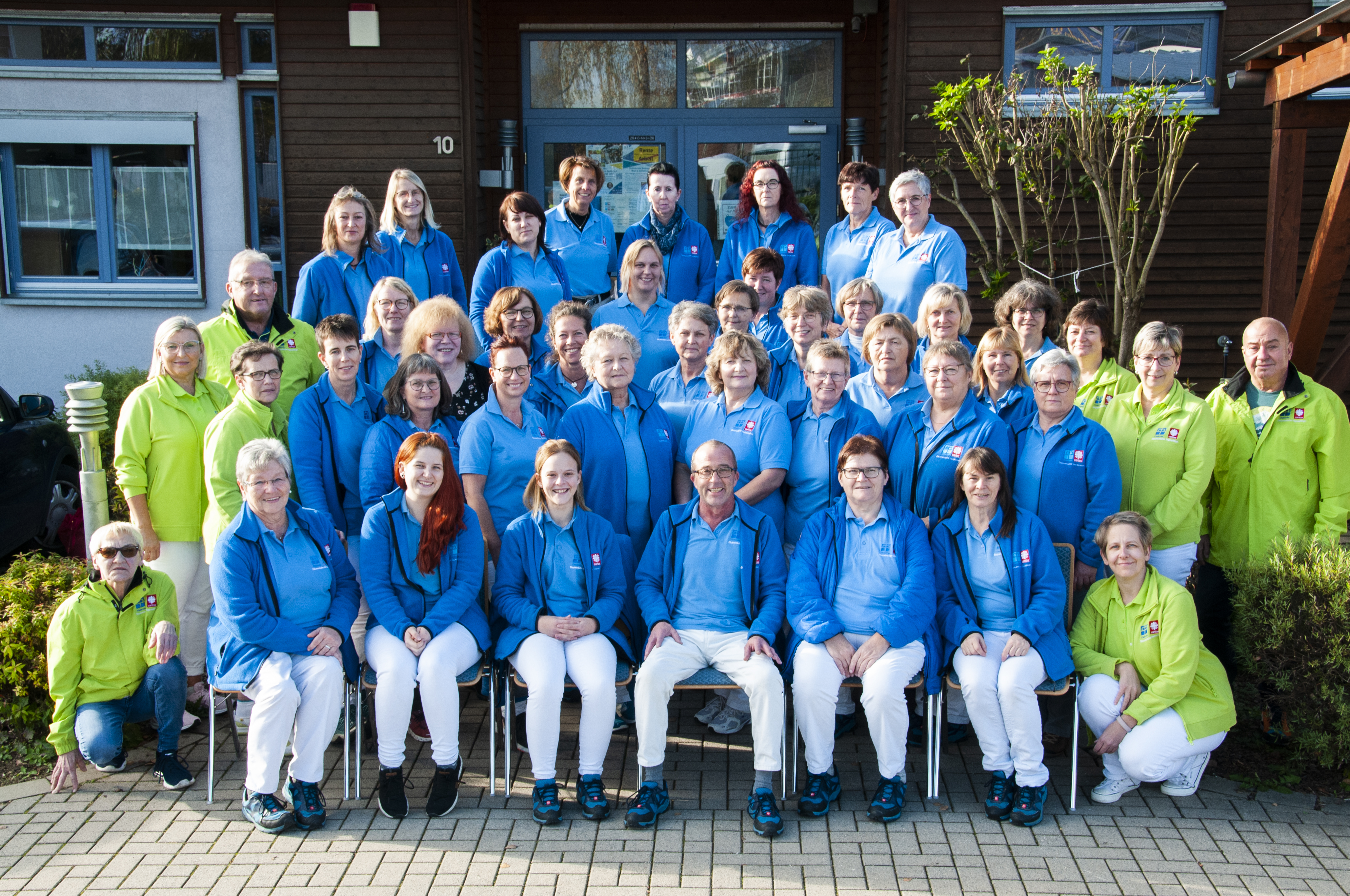 Angestellte der Sozialstation sitzen und stehen in mehreren Reihen hintereinander vor dem Eingang